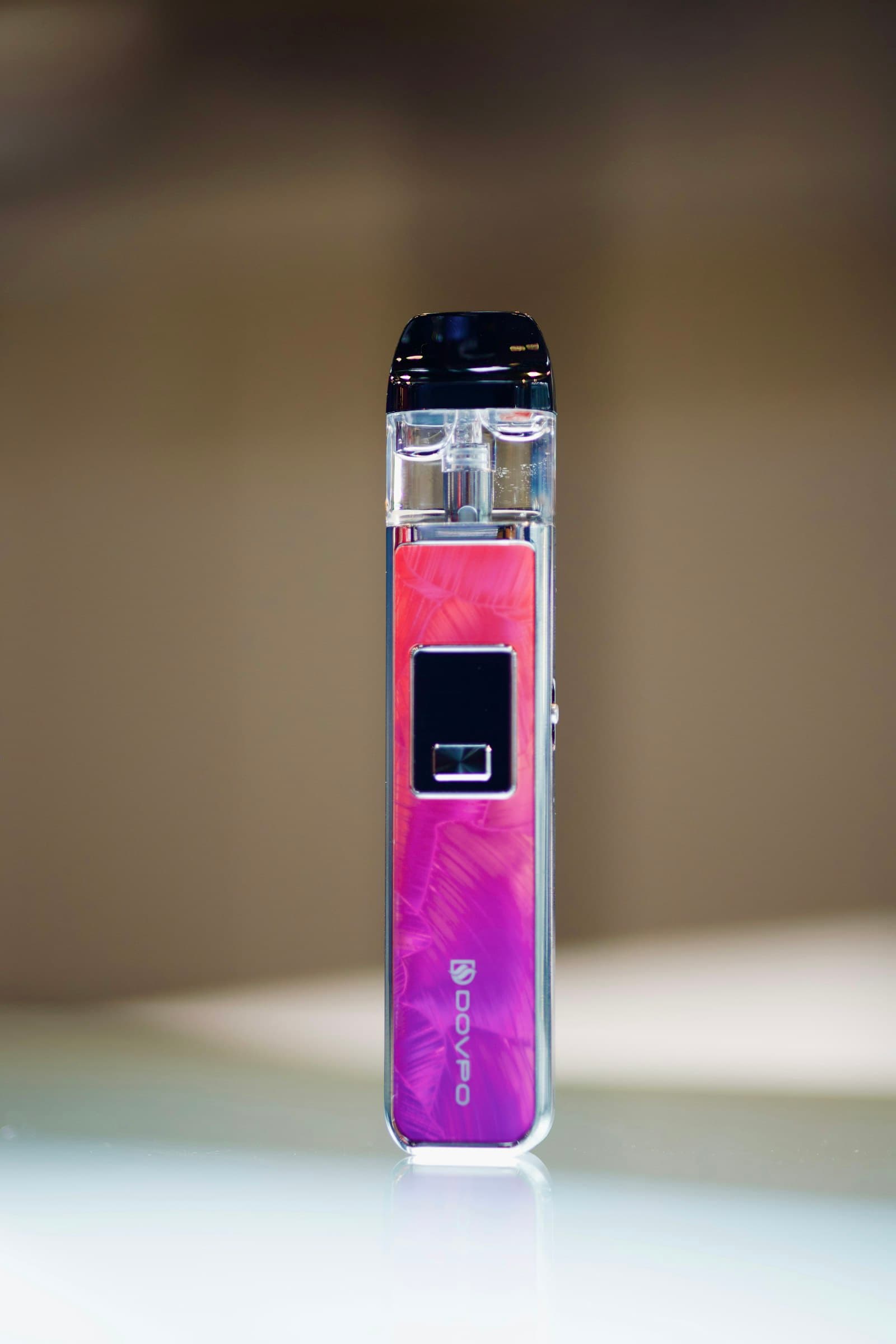 A purple and pink pod-system vape device standing upright on a reflective surface, showing its integrated display