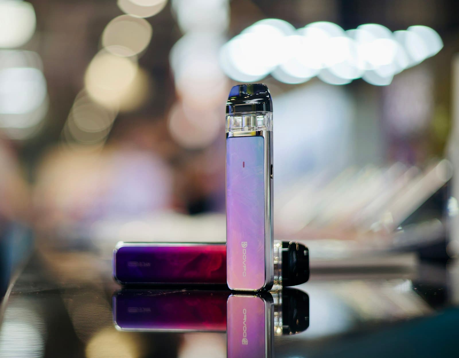 Two pod-system vape devices in different colourways, one standing and one lying flat, positioned together for comparison