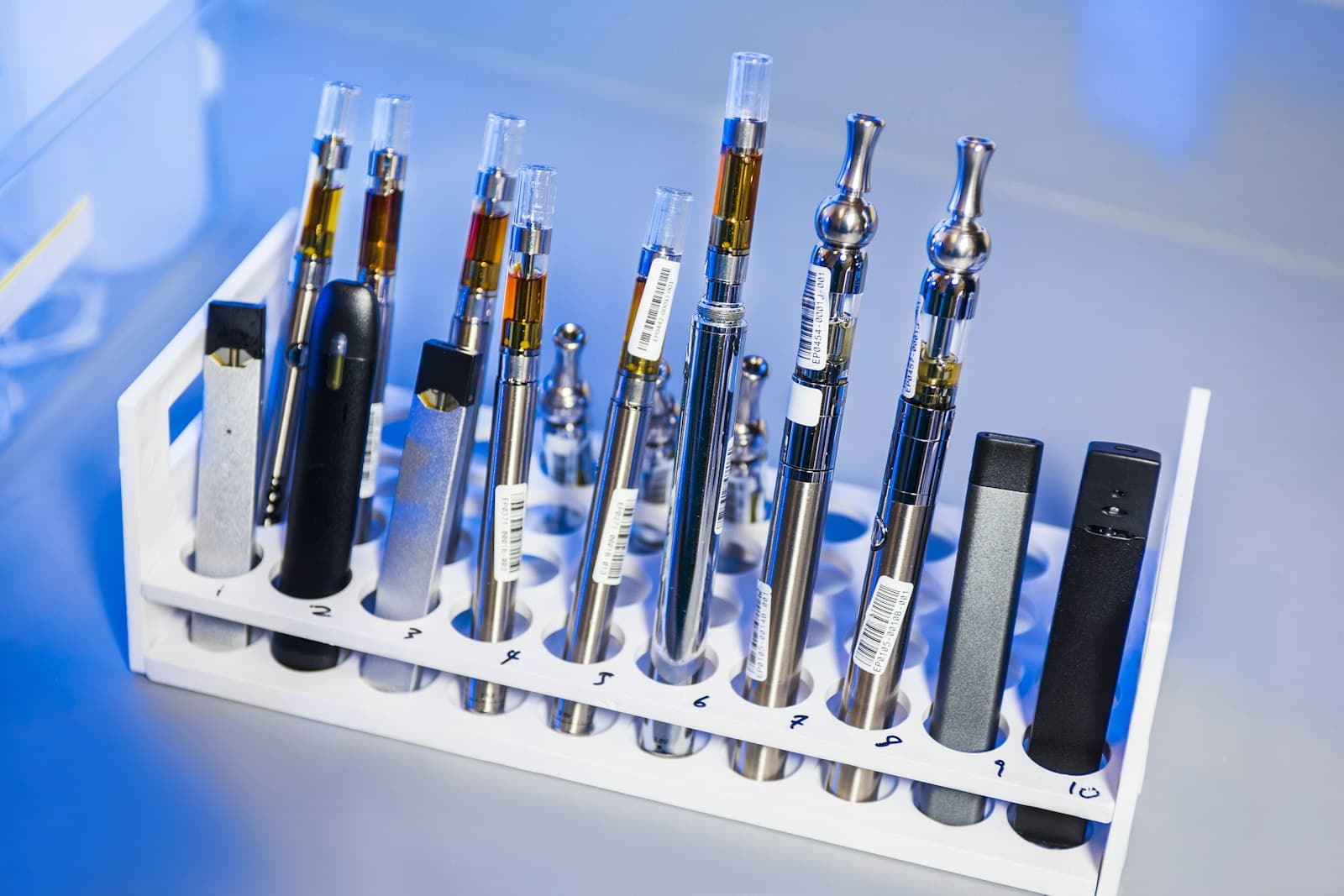 A row of small pod-system vape devices with visible e-liquid windows laid out on a table