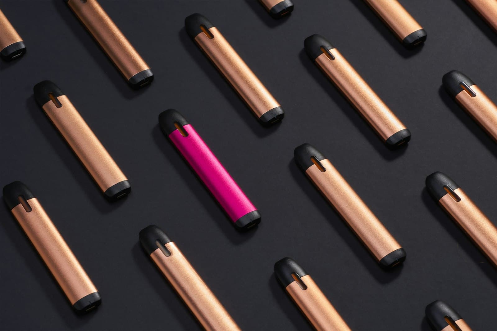 Several slim, pen-shaped rechargeable pod vape devices arranged in a diagonal pattern on a dark surface